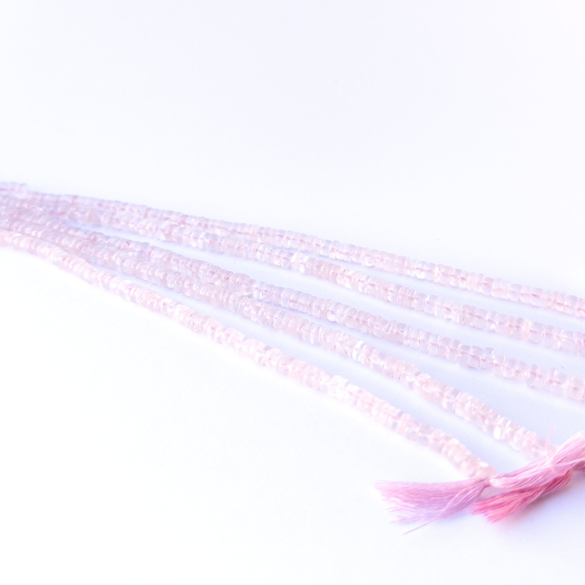 A person holds delicate strands of Rose Quartz beads, showcasing their smooth wheel design.