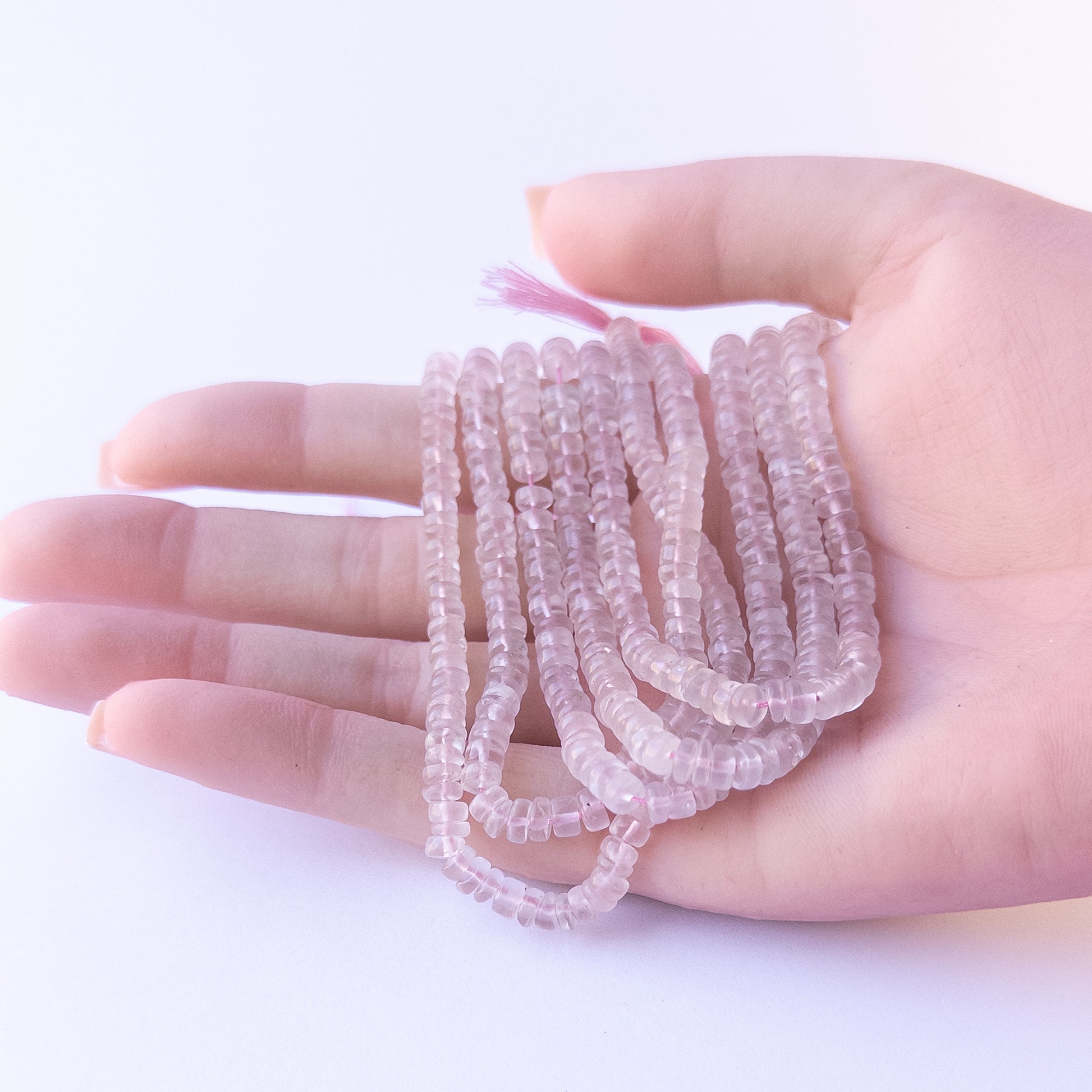 A person holds delicate strands of Rose Quartz beads, showcasing their smooth wheel design.