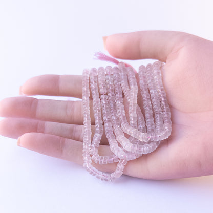 A person holds delicate strands of Rose Quartz beads, showcasing their smooth wheel design.