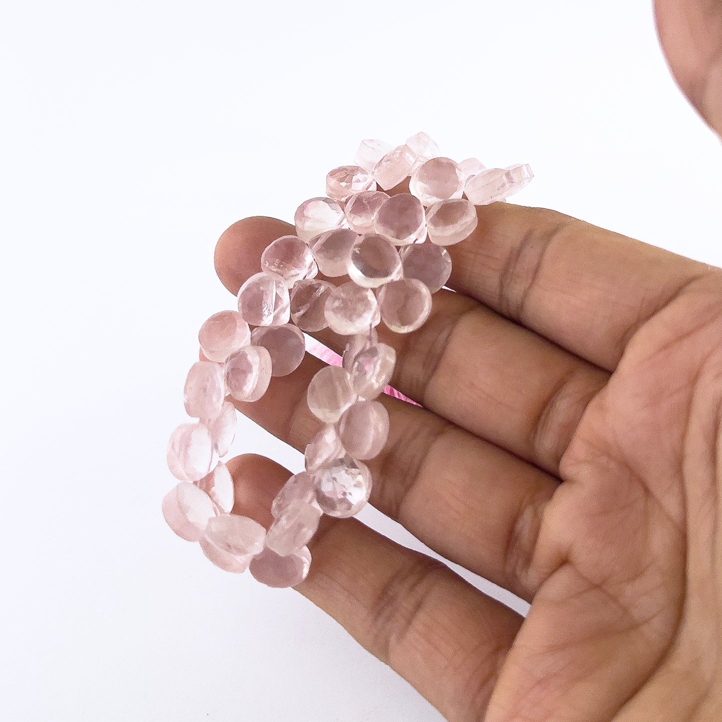 A person holds Rose Quartz briolette beads, showing their faceted teardrop design and pastel colour.