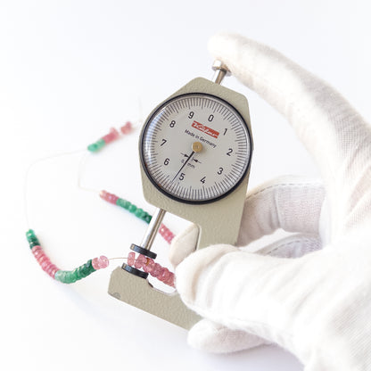 A dial gauge measures the Ruby and Emerald faceted rondelle 4.7–5.3mm gemstone.