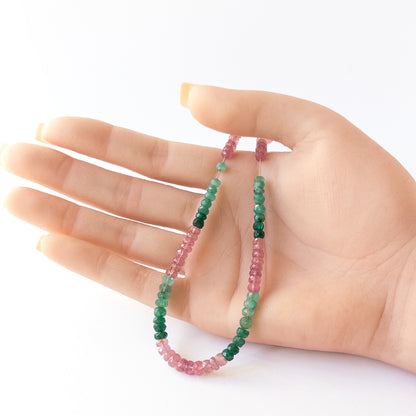 A person holds delicate strands of Ruby and Emerald beads, showcasing their faceted rondelle design.