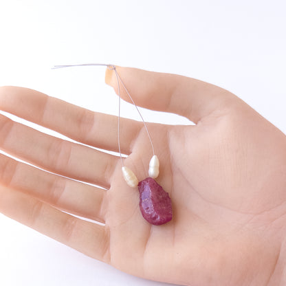A person holds delicate strands of Ruby and Freshwater Pearl beads, showcasing their rough‑drilled design.