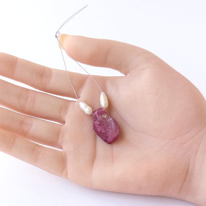A person holds delicate strands of Ruby and Freshwater Pearl beads, showcasing their rough‑drilled design.