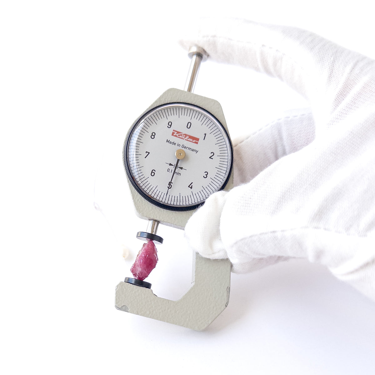 A dial gauge measures the Ruby rough‑drilled 21 × 15mm gemstone.