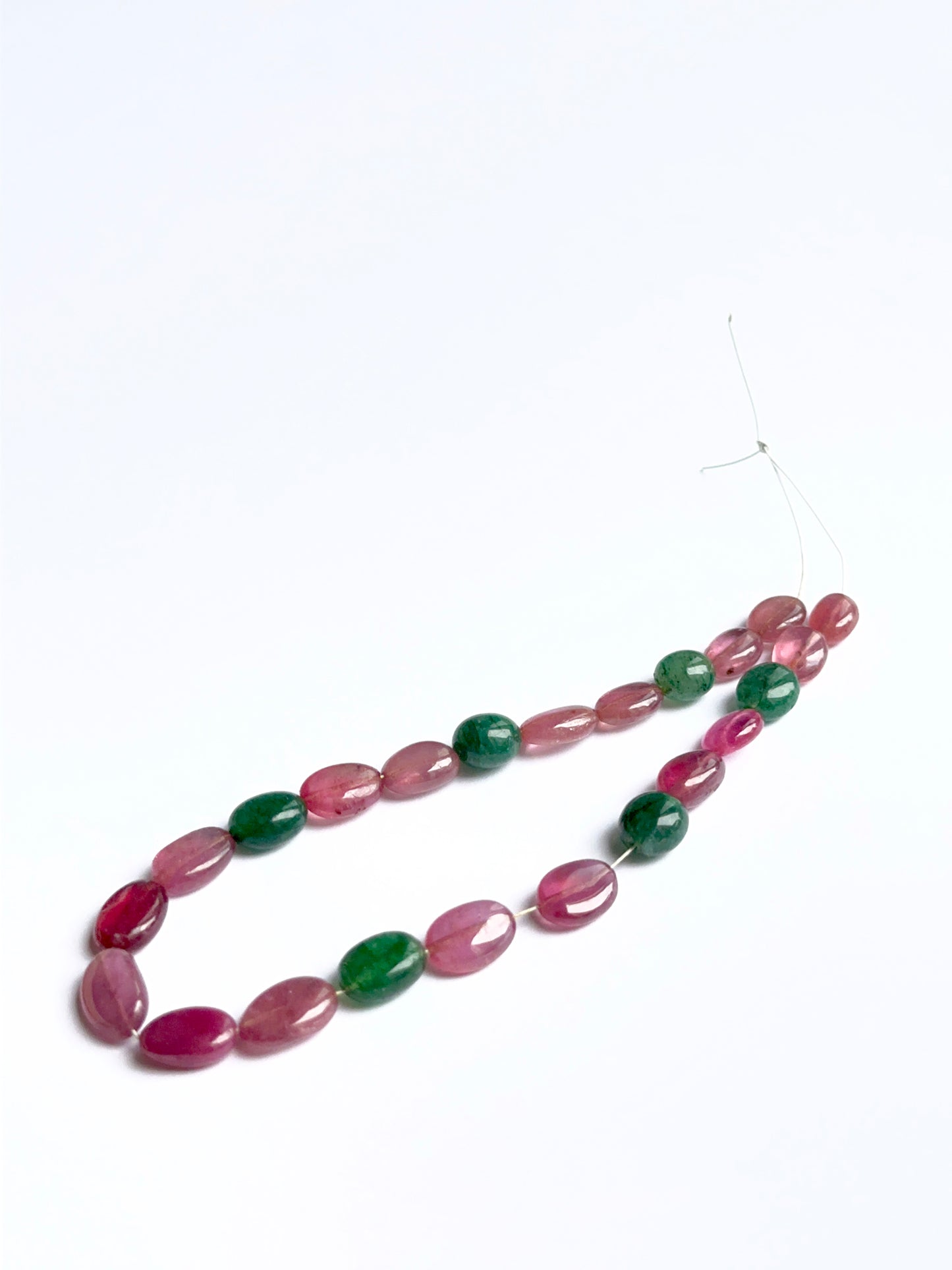 Smooth oval ruby and emerald beads arranged neatly to showcase gemstone quality and shine.