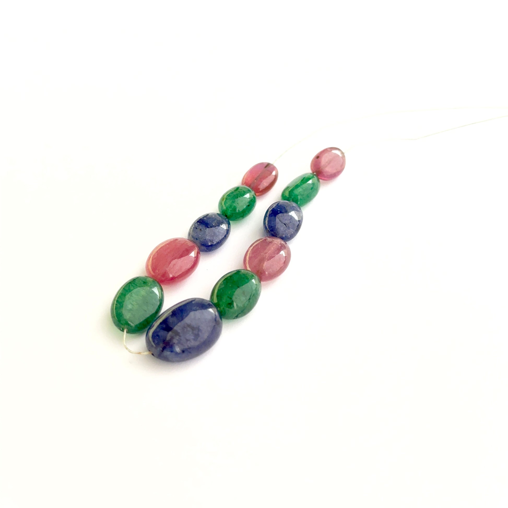 Smooth oval ruby, sapphire and emerald beads arranged neatly to showcase gemstone quality.