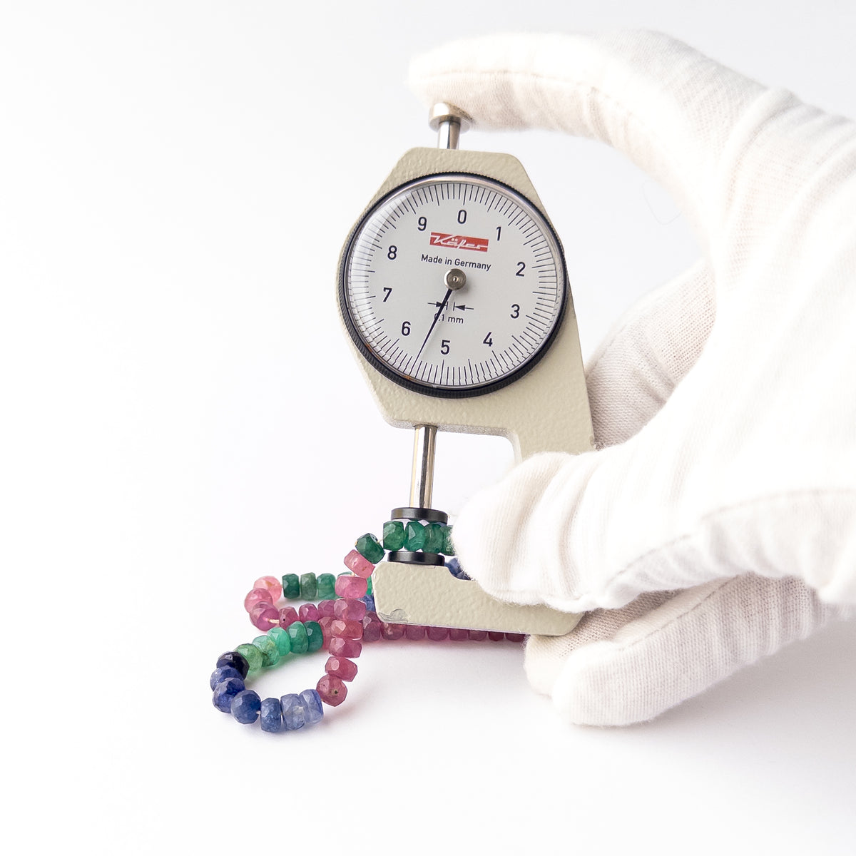 A dial gauge measures the Multi Precious Ruby Blue Sapphire and Emerald Faceted Rondelle 5-6mm gemstone.