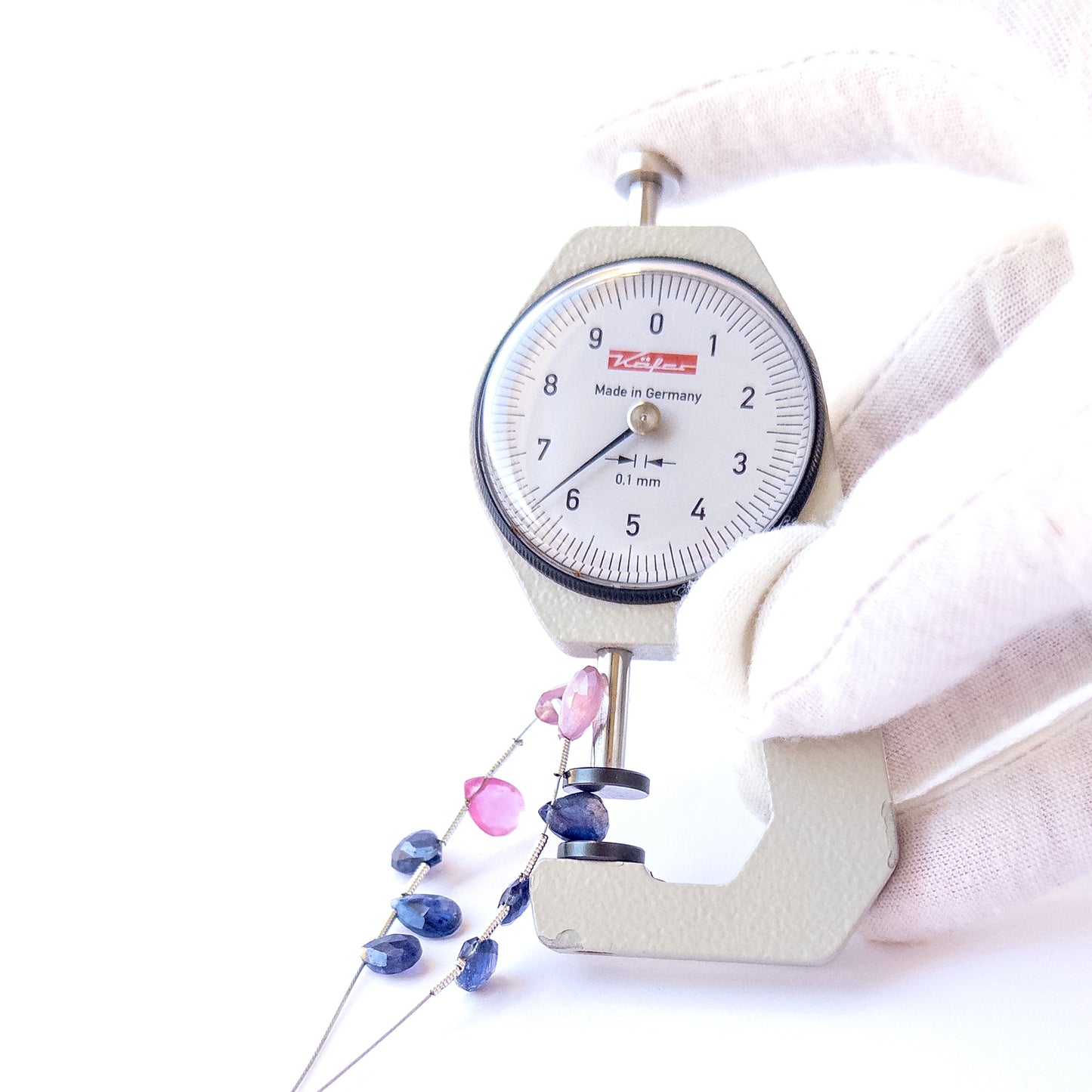 A dial gauge measures the Ruby and Blue Sapphire faceted briolette 5.7–9.7mm gemstone.