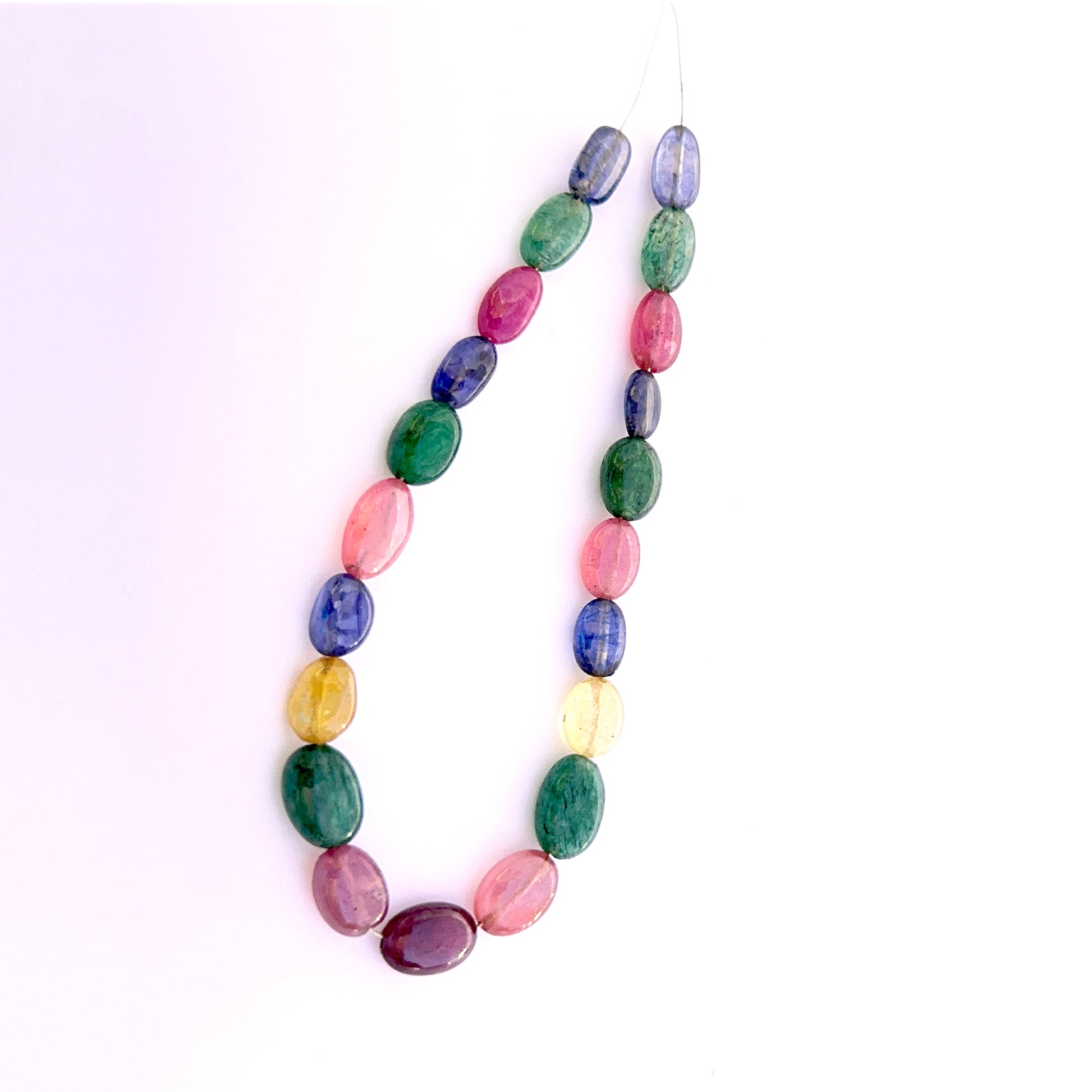 Smooth oval ruby, blue sapphire, yellow sapphire and emerald beads arranged to display uniform shape and rich gemstone hues.
