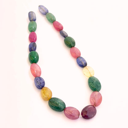 Close‑up of mixed ruby, blue sapphire, yellow sapphire and emerald smooth oval beads showing polished surfaces and vivid colours.
