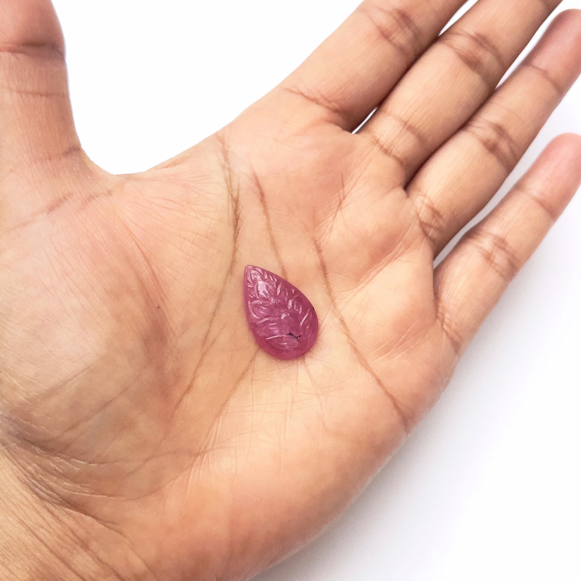 A person holds delicate strands of ruby beads, showcasing their carved design.