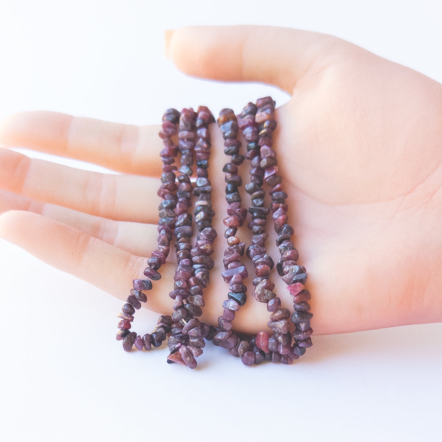 A person holds delicate strands of Ruby chip beads, highlighting their organic design.