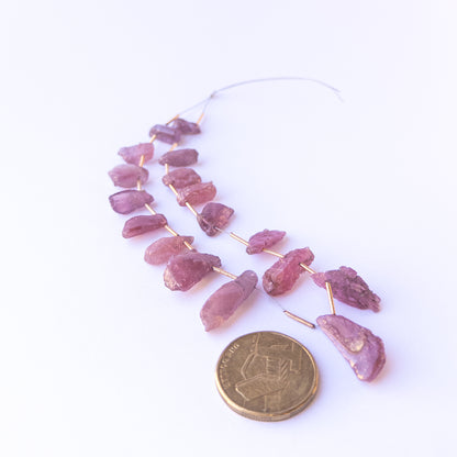 A coin is placed near delicate pieces of Ruby rough beads for scale.