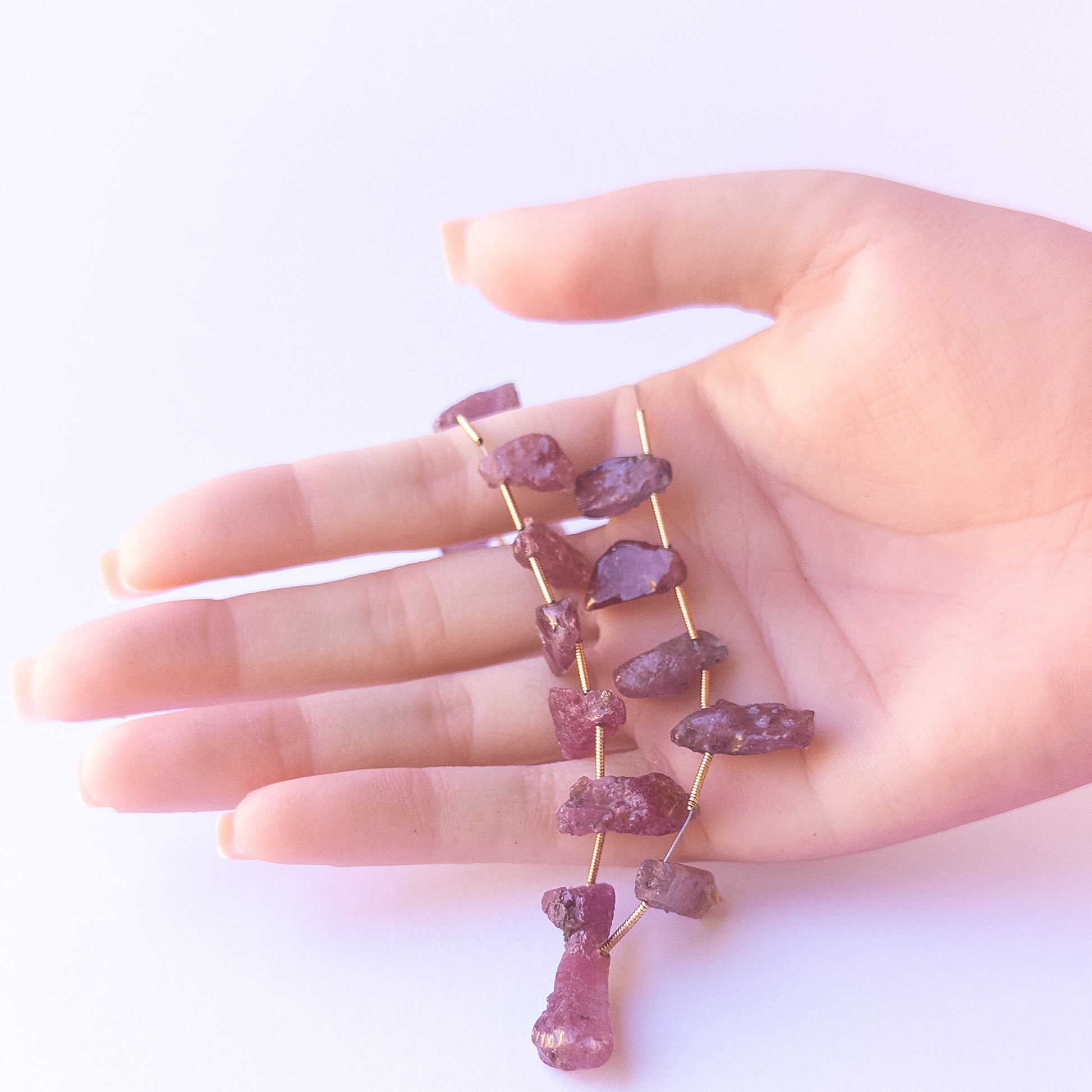 A person holds delicate pieces of Ruby rough beads, showcasing their drilled rough design.