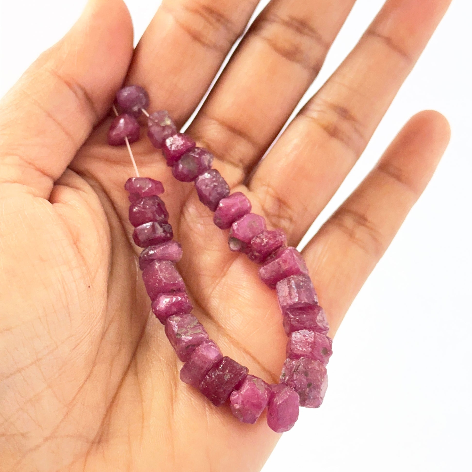 A person holds delicate strands of Ruby beads, showcasing their smooth design.