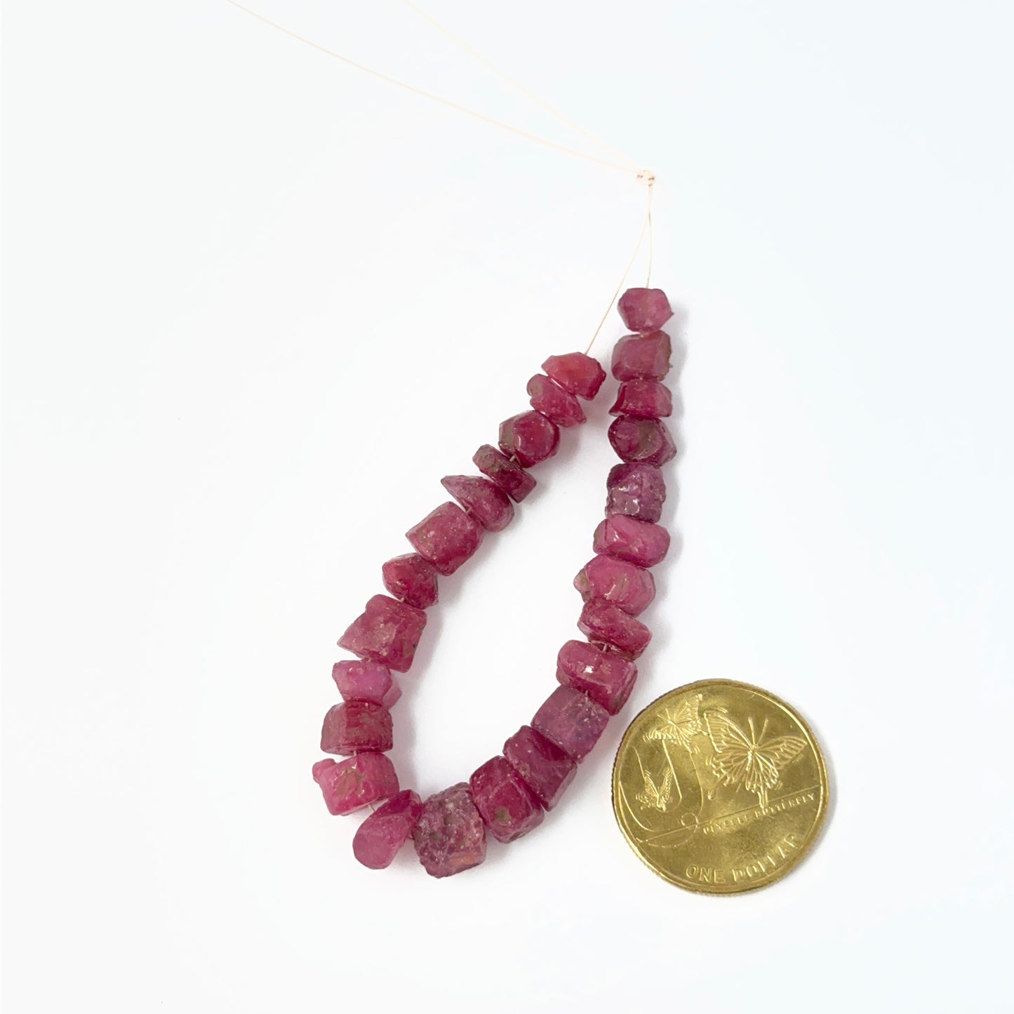 Stone beads made from Ruby rough pieces with drilled centres and raw finish placed next to a australian dollar coin for scale.