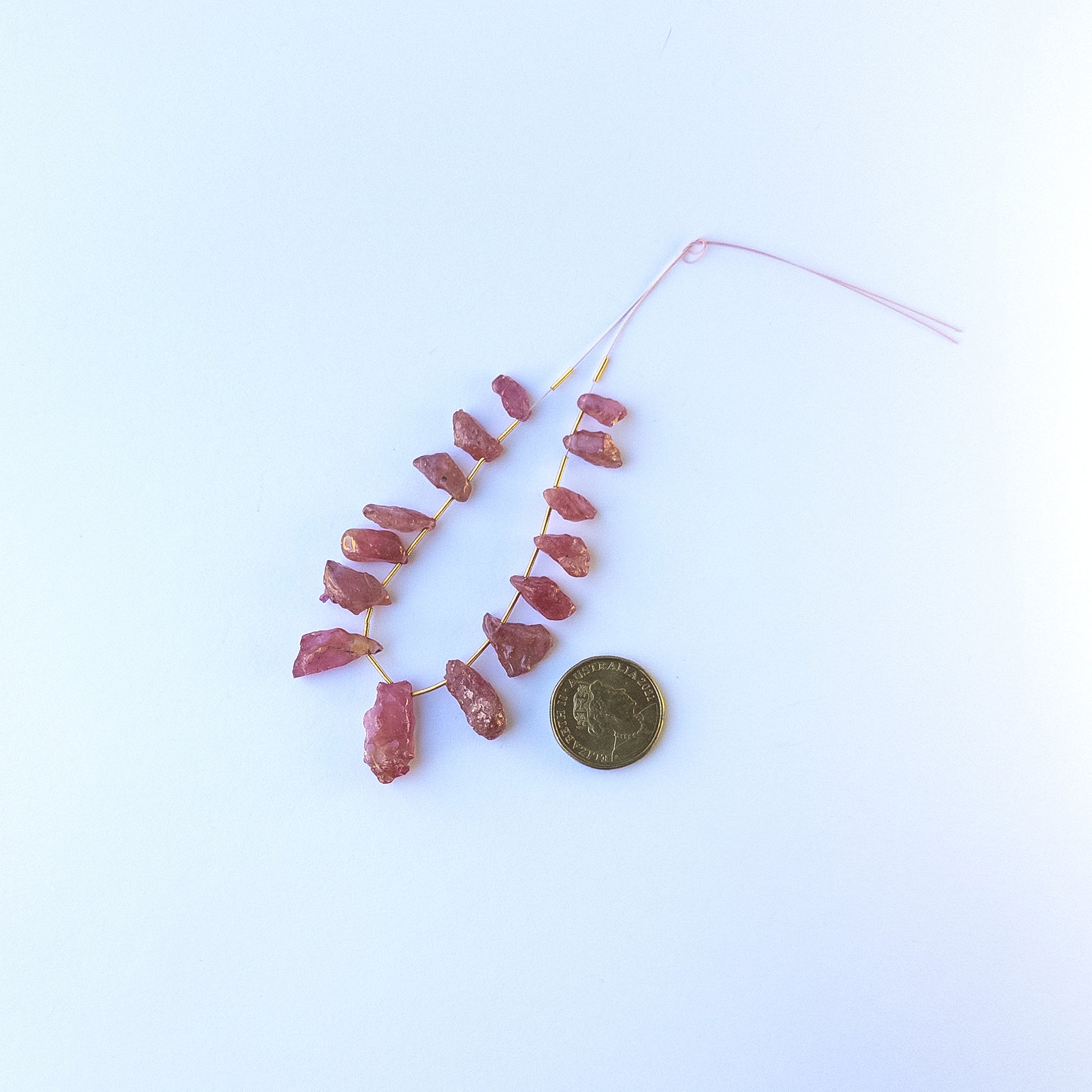 A coin is placed near delicate pieces of Ruby rough beads for scale.