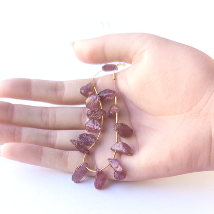 A person holds delicate strands of Ruby drilled rough beads, showcasing their natural rough design.