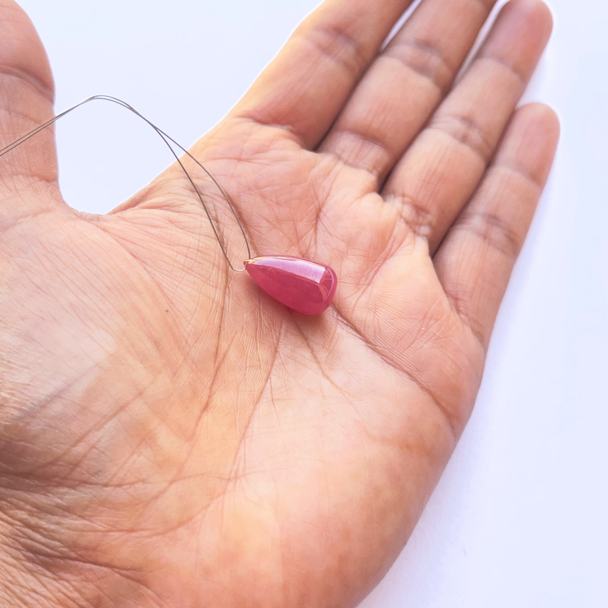 A person holds delicate  ruby bead, showcasing their smooth design.