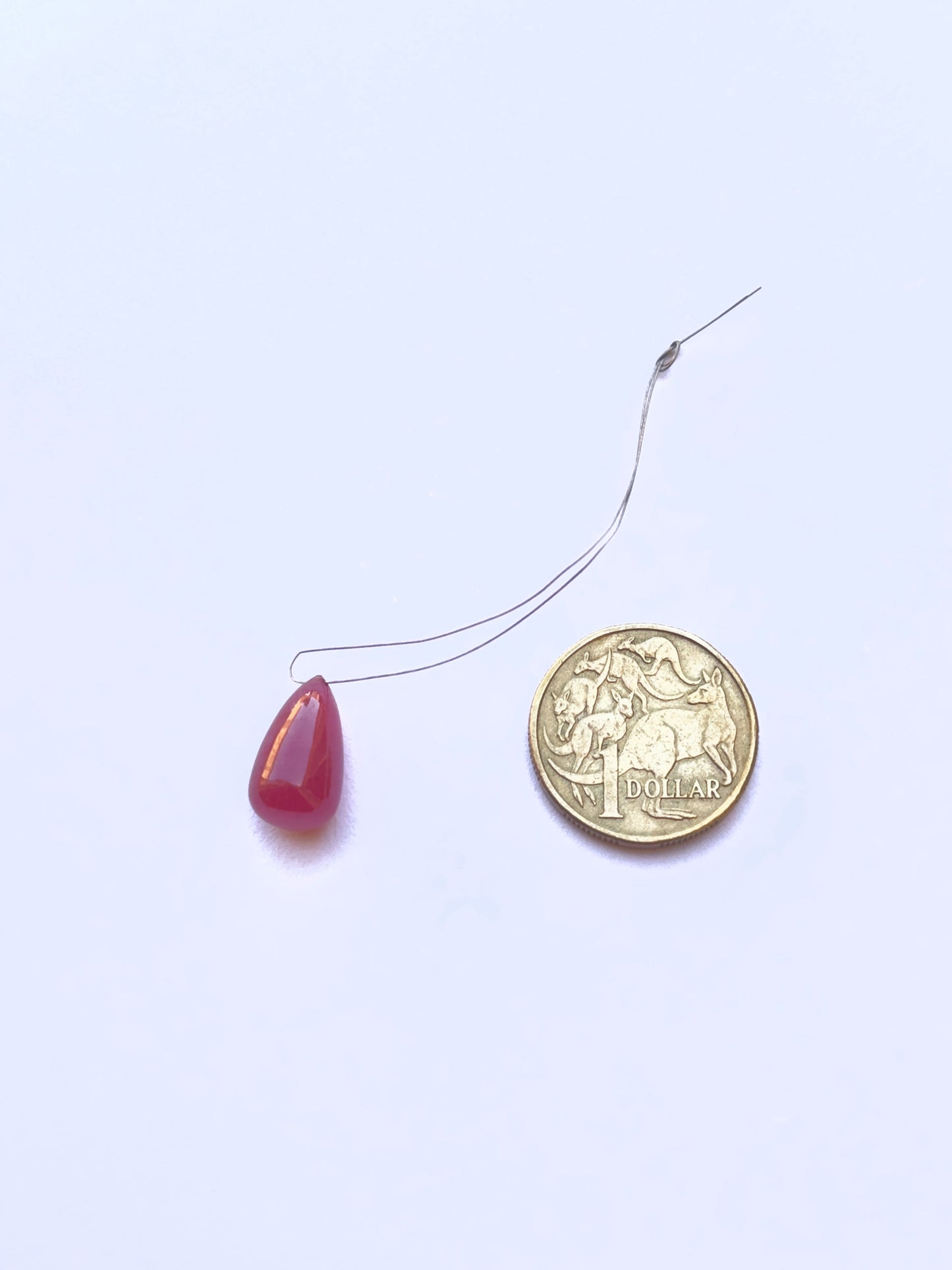 A coin besides the ruby teardrop smooth  gemstone.