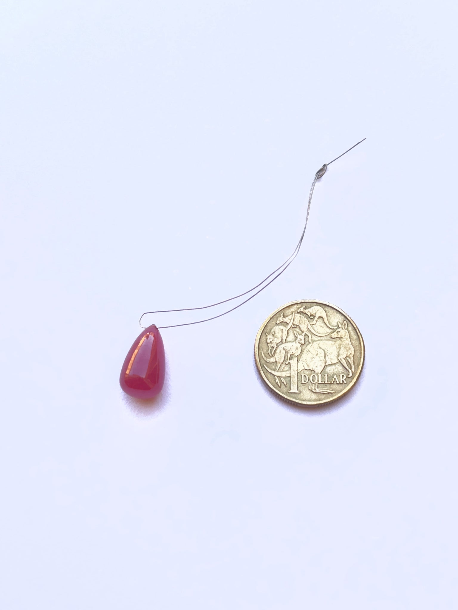 A coin besides the ruby teardrop smooth  gemstone.