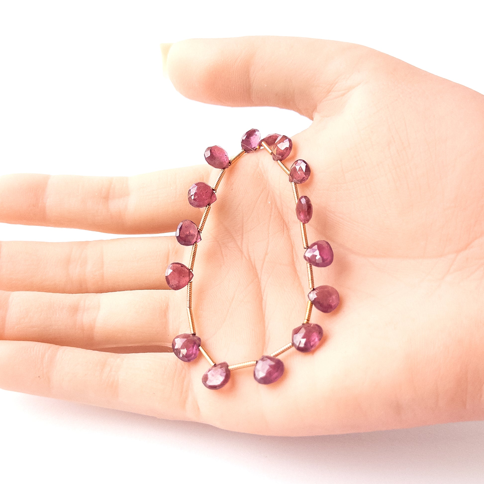 A person holds delicate strands of Ruby beads, showcasing their faceted briolette design.