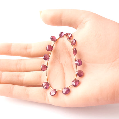 A person holds delicate strands of Ruby beads, showcasing their faceted briolette design.