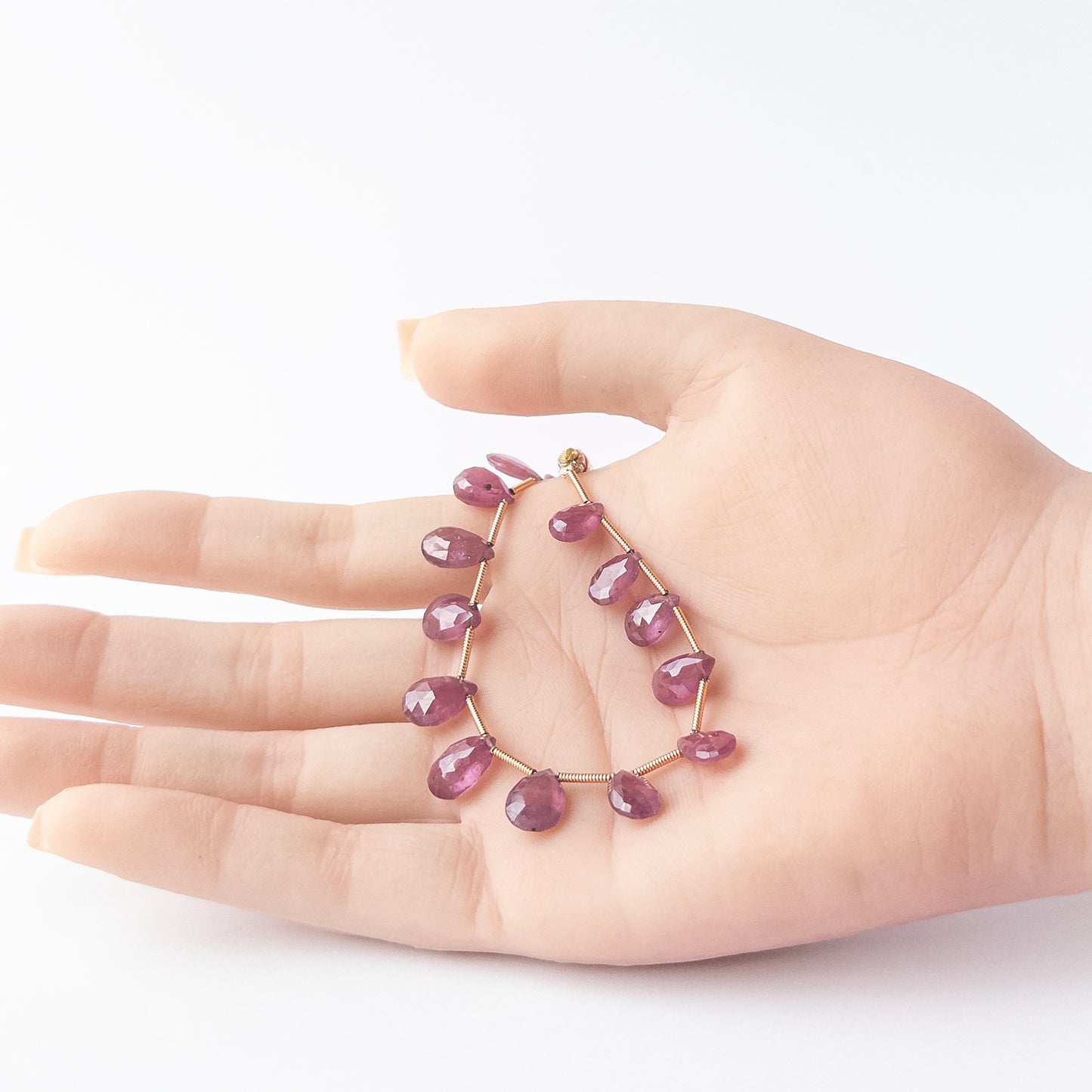 A person holds delicate strands of Ruby beads, showcasing their faceted briolette design.