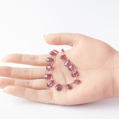 A person holds delicate strands of Ruby beads, showcasing their faceted briolette design.