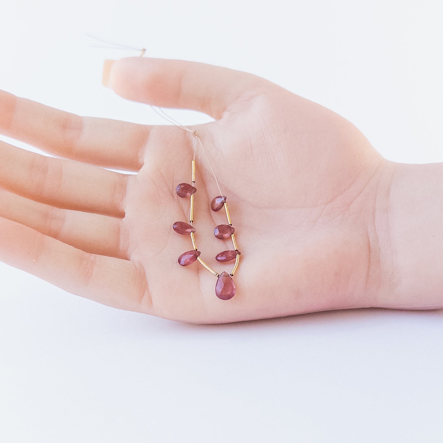 A person holds delicate strands of Ruby faceted briolette beads, showcasing their cut design.
