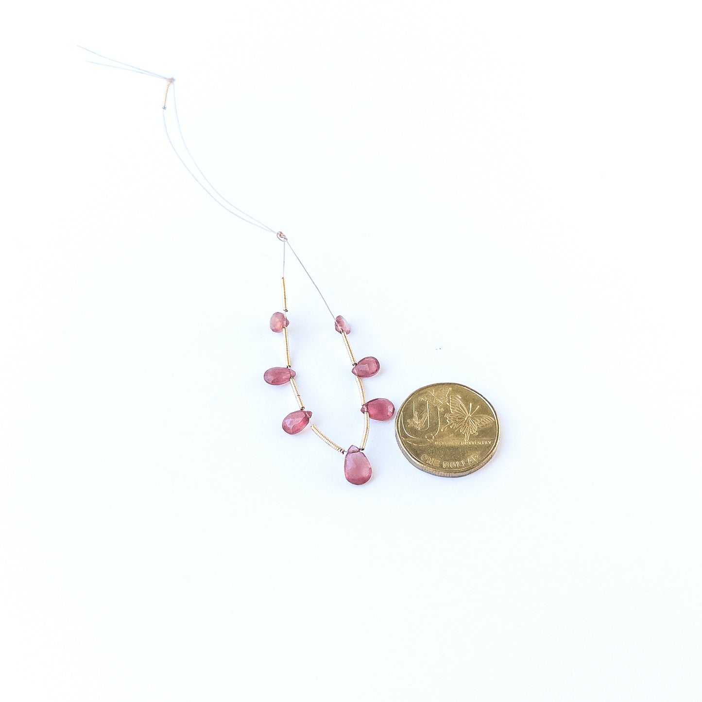 A coin is placed near delicate pieces of Ruby faceted briolette beads for scale.