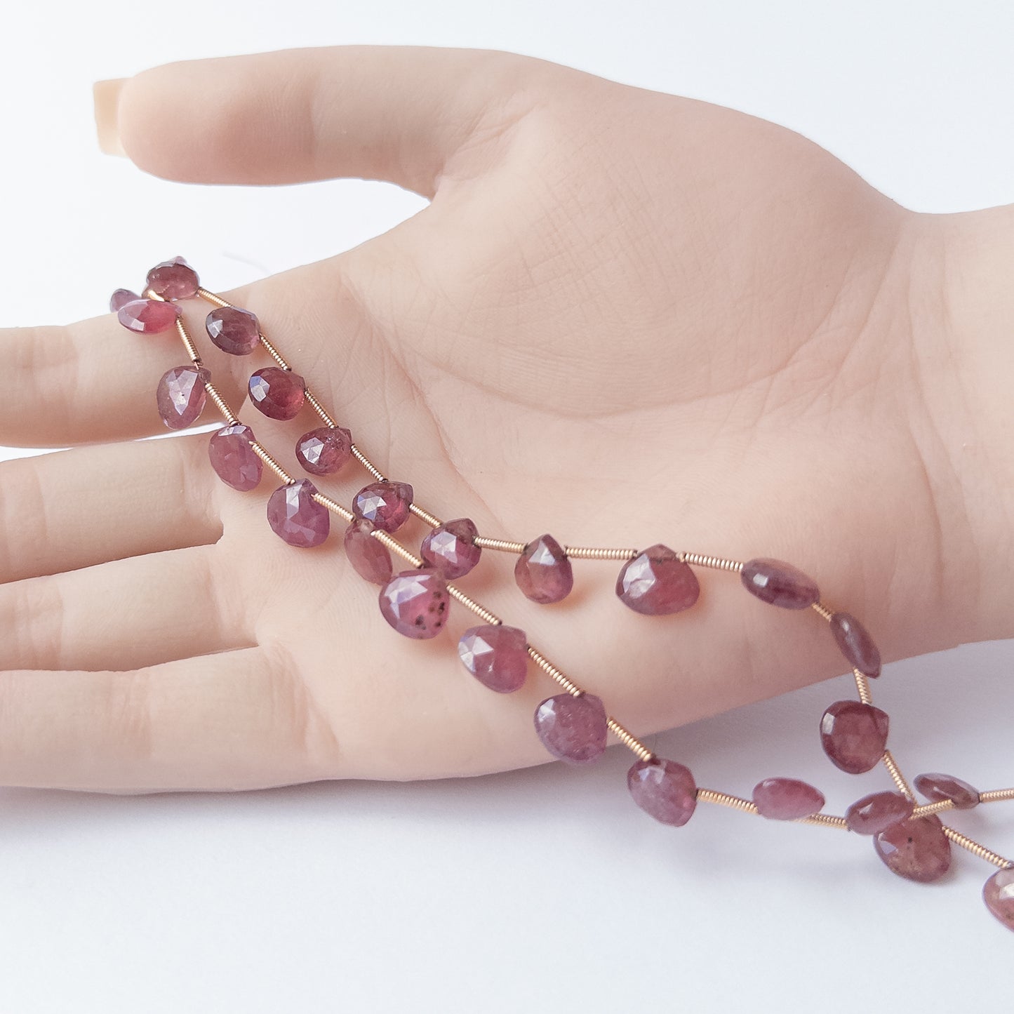 A person holds delicate strands of Ruby beads, showcasing their faceted briolette design.