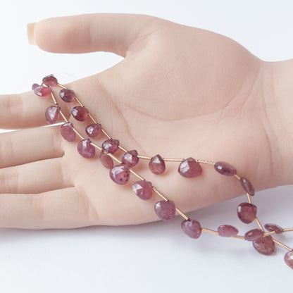 A person holds delicate strands of Ruby beads, showcasing their faceted briolette design.