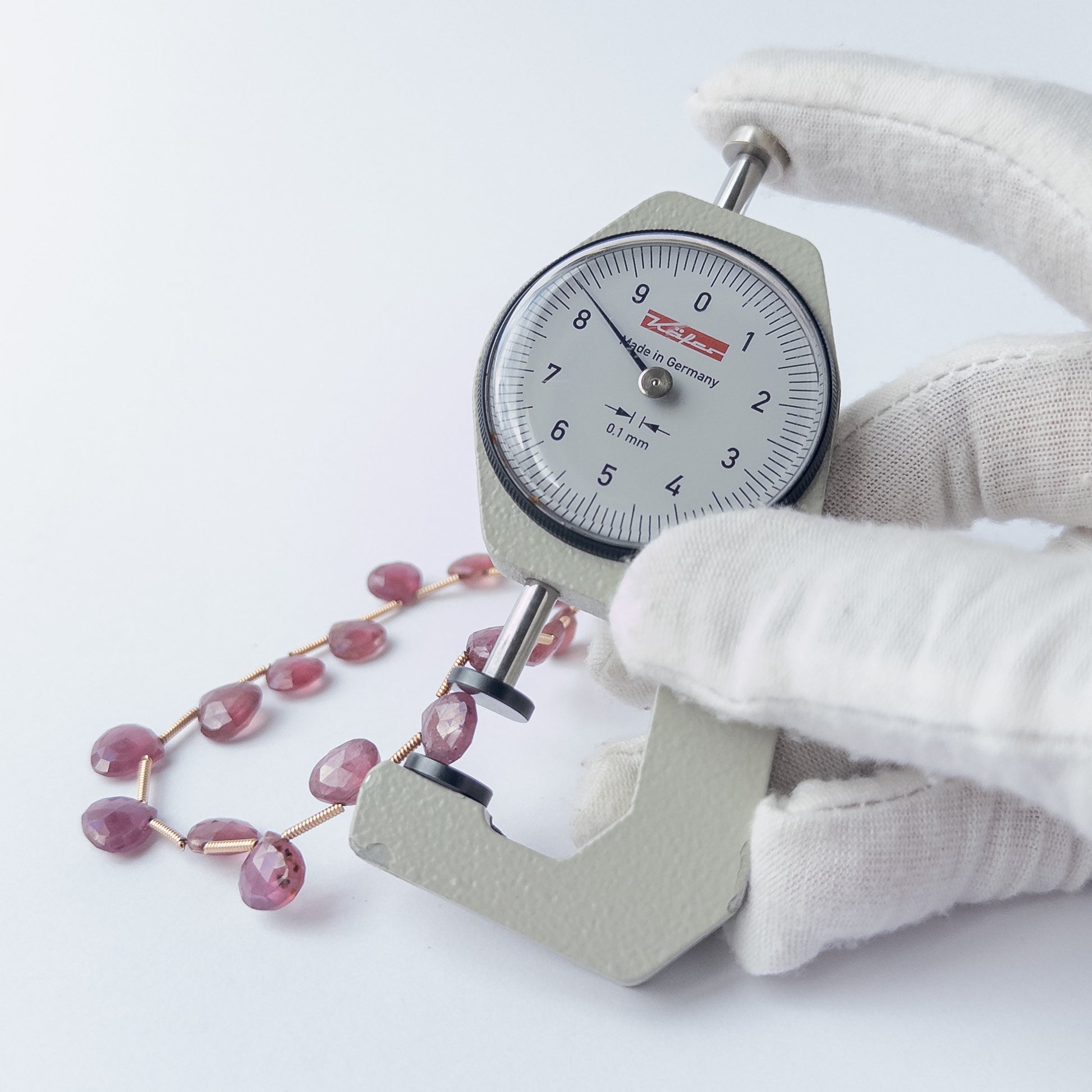 A dial gauge measures the Ruby faceted briolette 7.5–8.5mm bead size gemstone.
