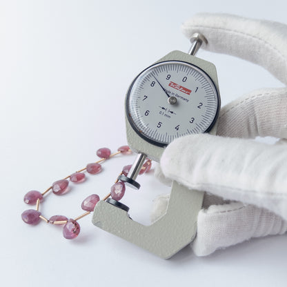 A dial gauge measures the Ruby faceted briolette 7.5–8.5mm bead size gemstone.