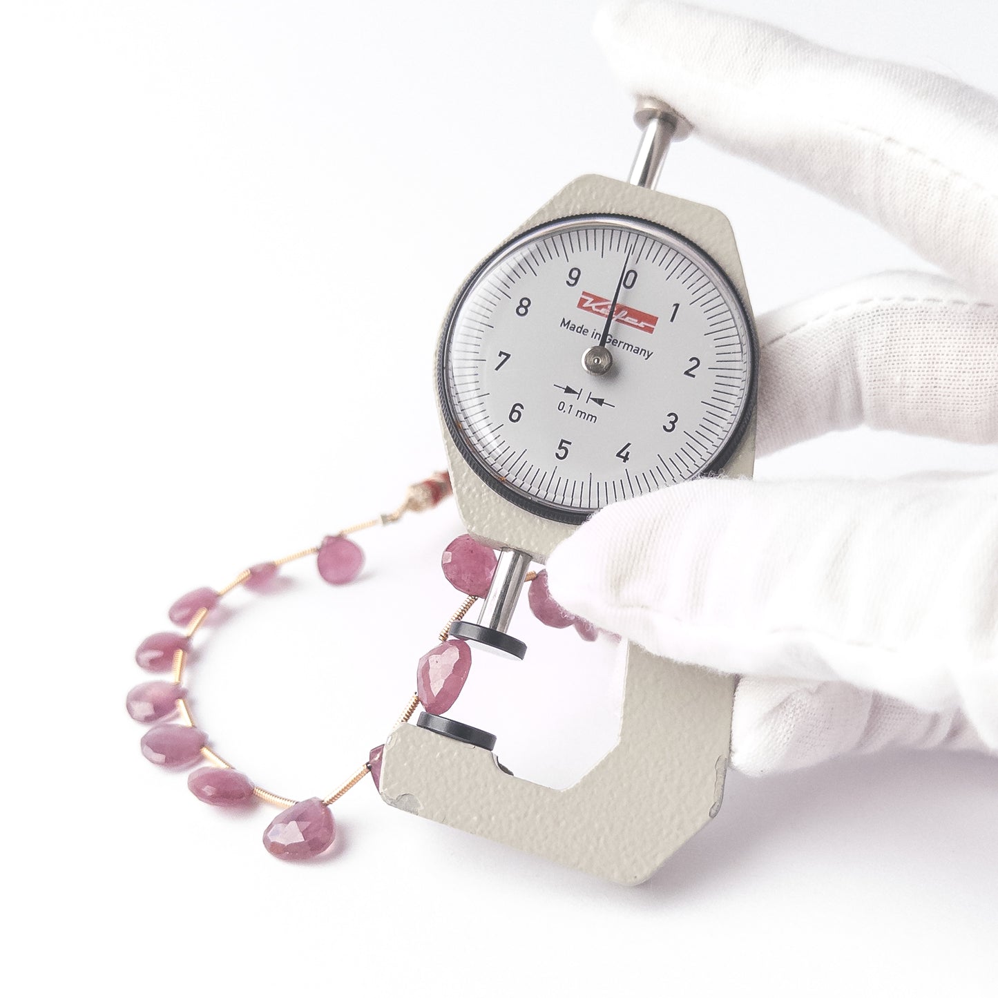 A dial gauge measures the Ruby faceted briolette 8–9.3mm bead size gemstone.