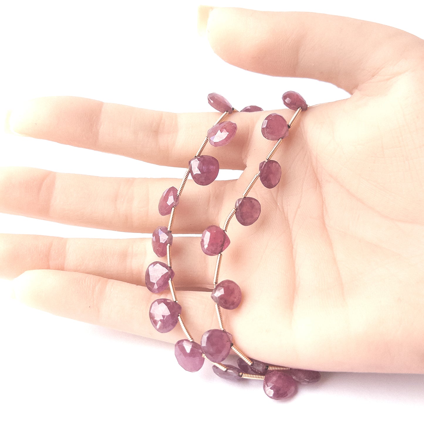 A person holds delicate strands of Ruby beads, showcasing their faceted briolette design.