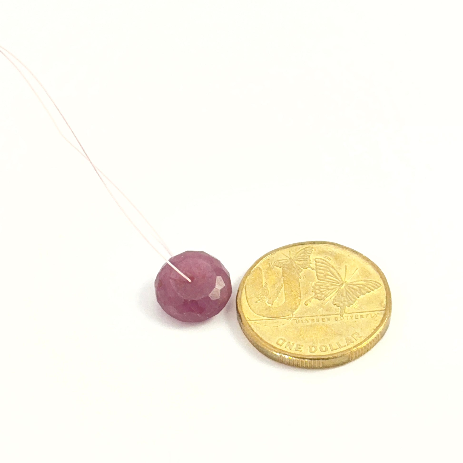 Polished Ruby disc gemstone bead, deep red colour, 12.3mm size placed next to a coin for scale.