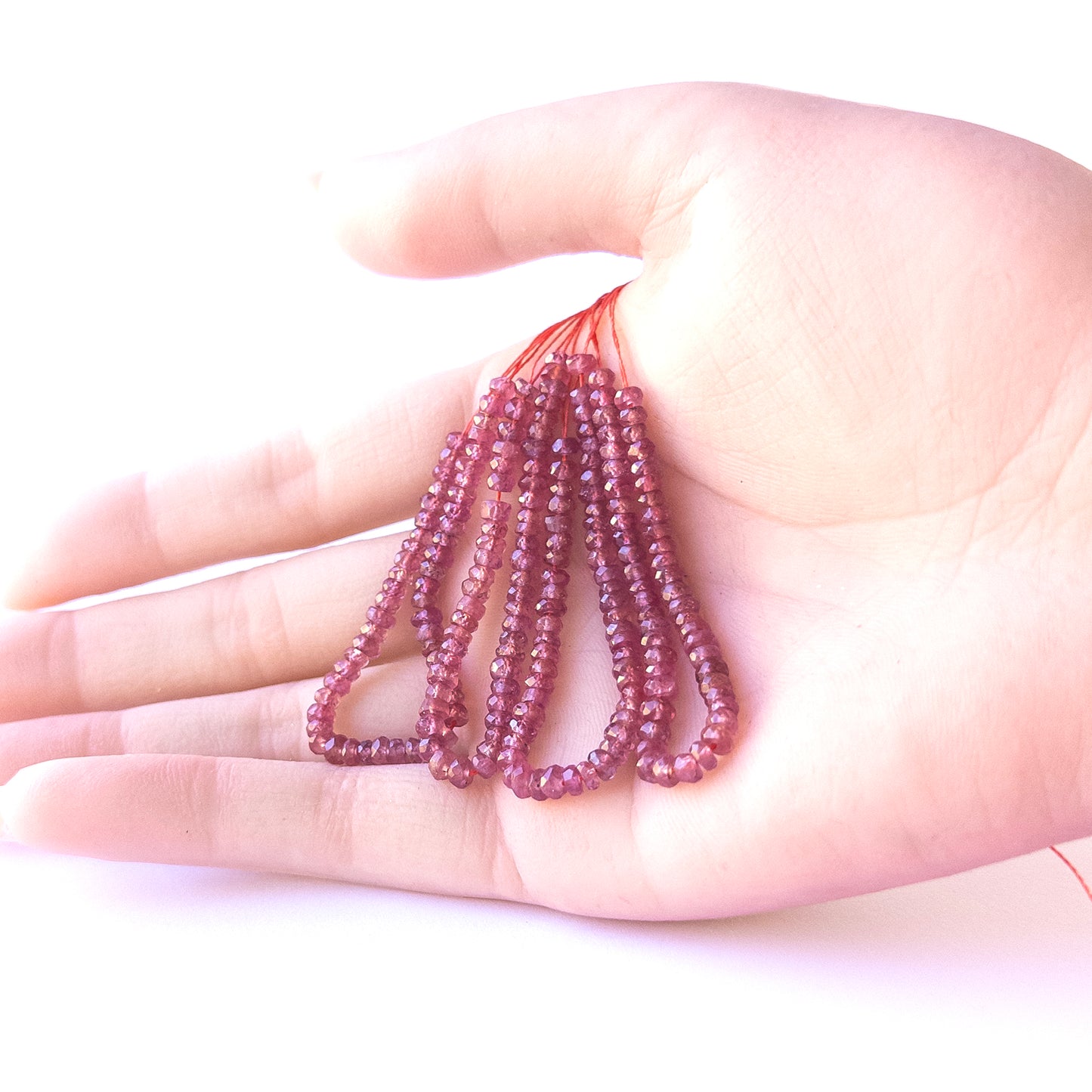 A person holds delicate strands of Ruby beads, showcasing their Faceted Rondelle design.