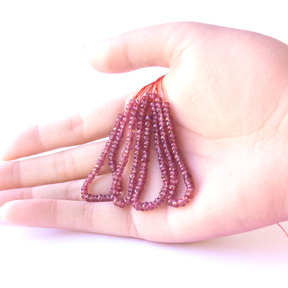 A person holds delicate strands of Ruby beads, showcasing their Faceted Rondelle design.