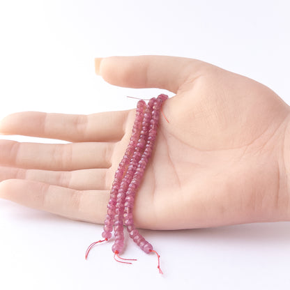 A person holds delicate strands of Ruby beads, showcasing their faceted rondelle design.
