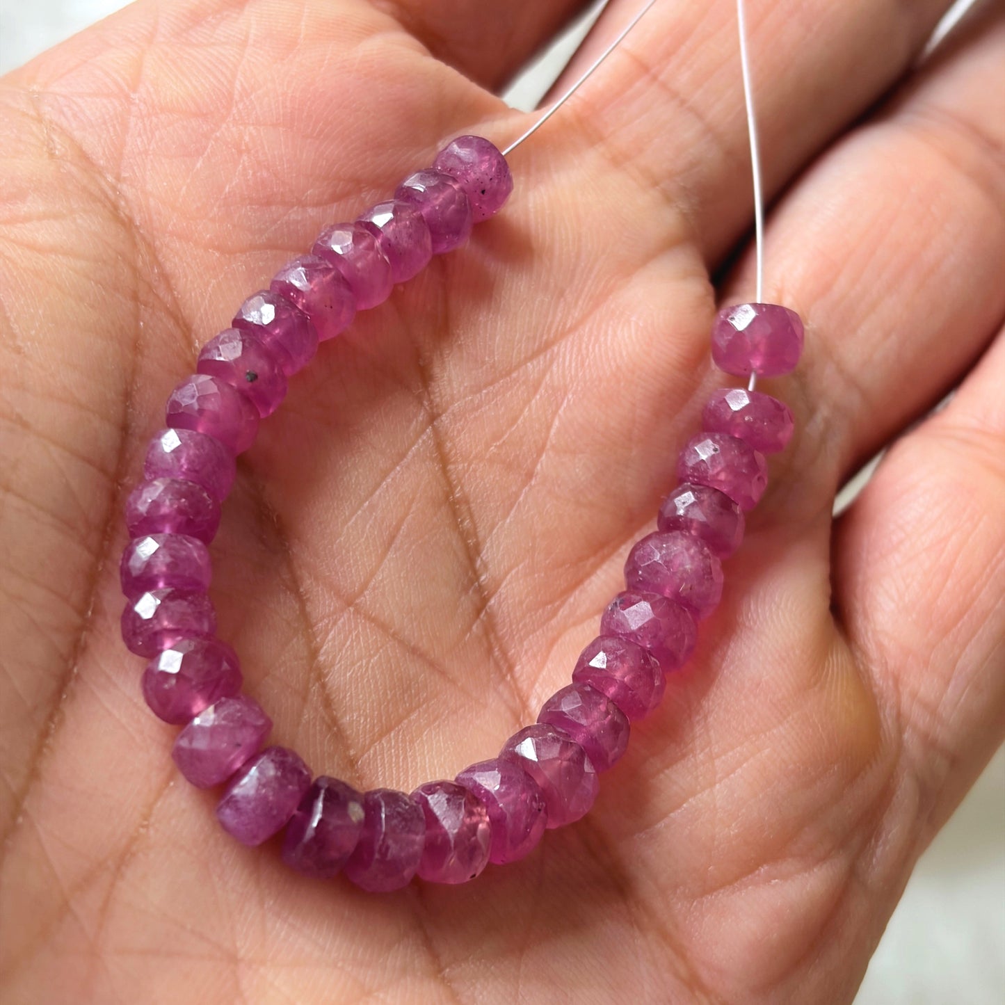 A person holds delicate strands of ruby beads, showcasing their faceted design