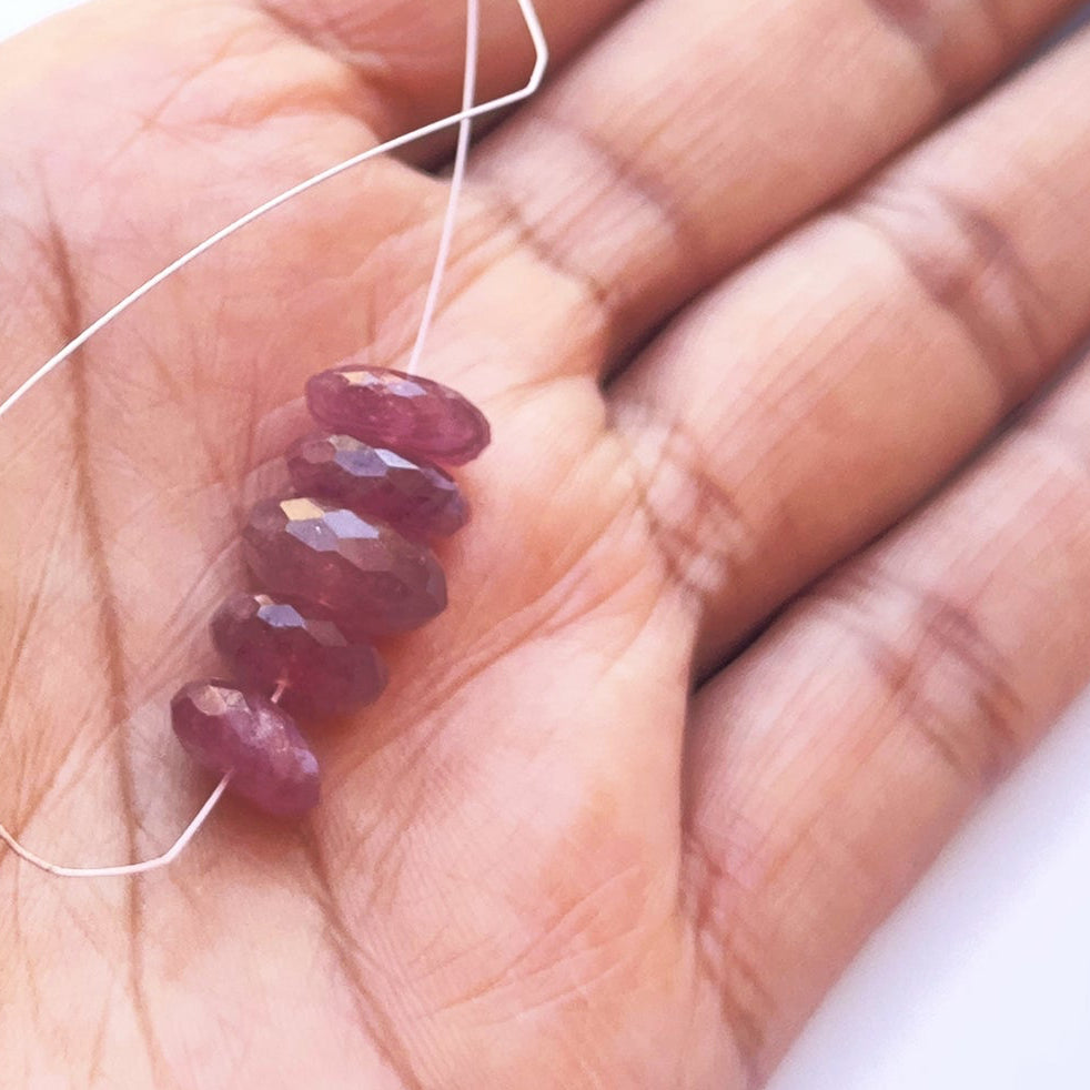 A person holds delicate strands of ruby beads, showcasing their faceteddesign.