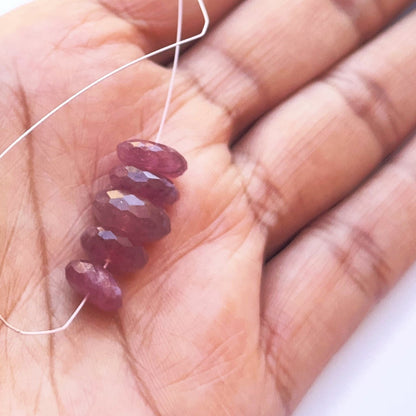 A person holds delicate strands of ruby beads, showcasing their faceteddesign.