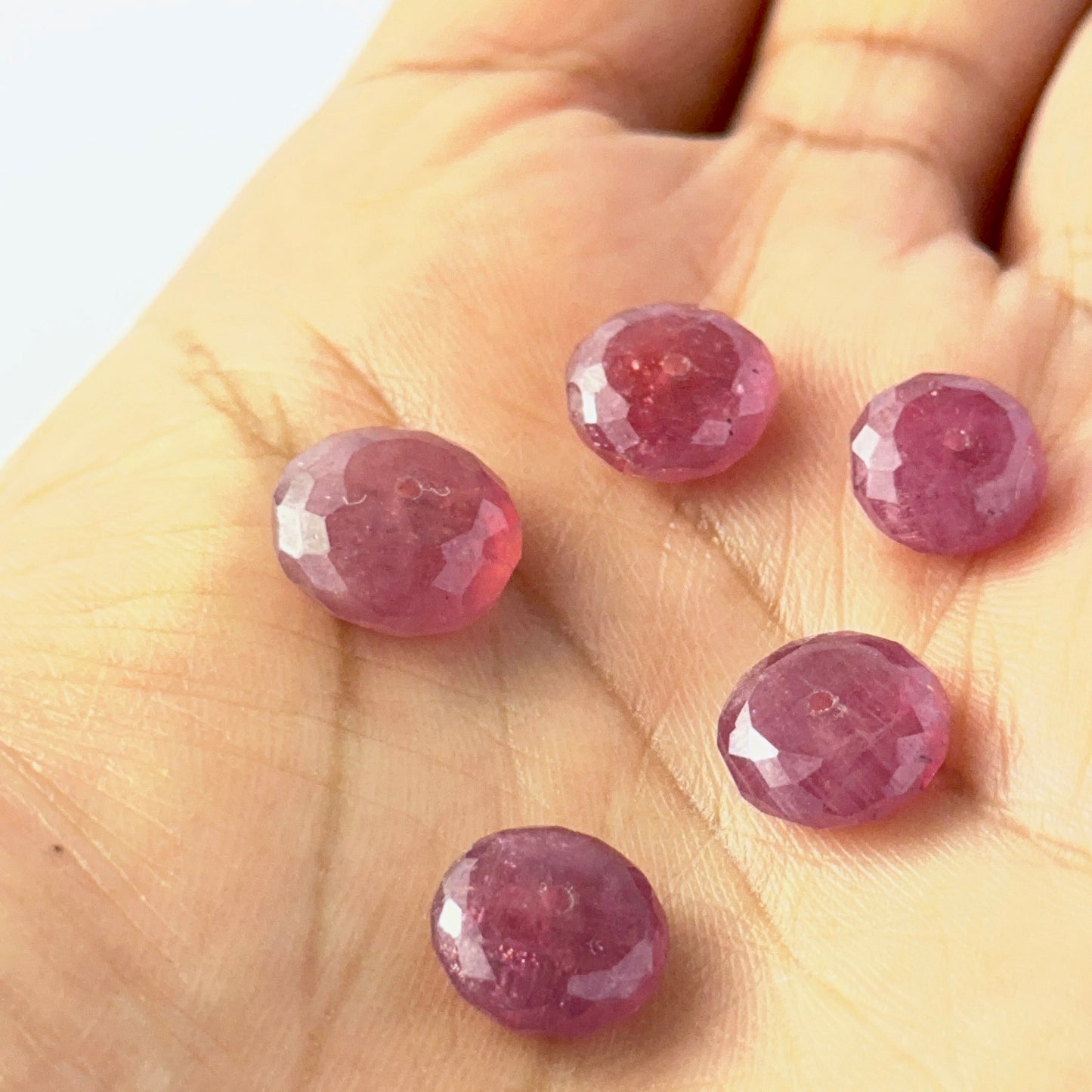 A person holds delicate Ruby beads, showcasing their faceted rondelle design