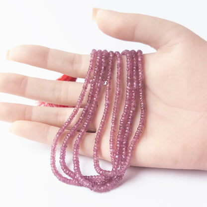 A person holds delicate strands of Ruby beads, showcasing their faceted rondelle design.