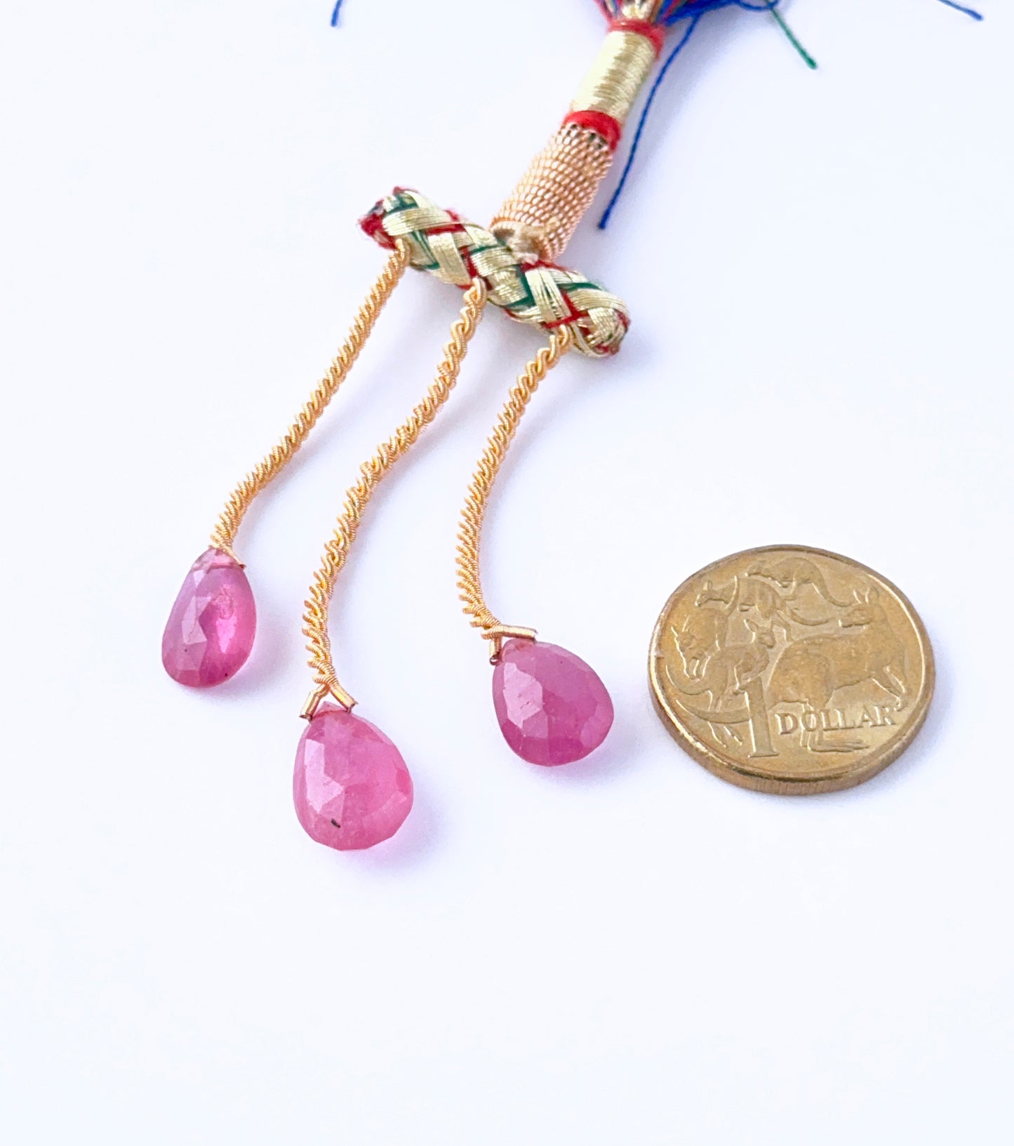 A Australian dollar coin  places next to the Ruby faceted teardrop 13–16mm gemstone for scale.