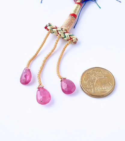 A Australian dollar coin  places next to the Ruby faceted teardrop 13–16mm gemstone for scale.