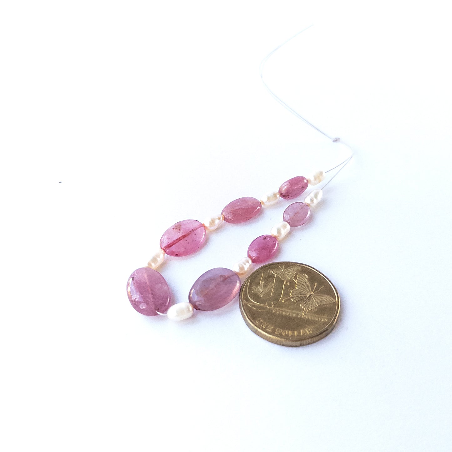 A coin is placed near Ruby and freshwater pearl beads for scale comparison.